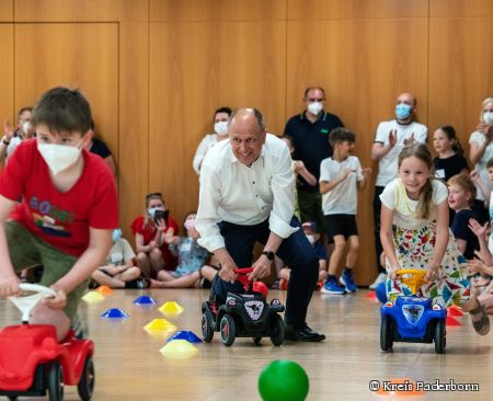Der Landrat macht ein Bobbycarwettrennen mit den Kindern der Grundschule.