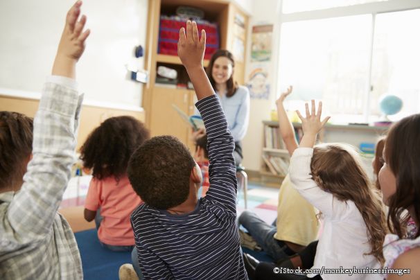 Kinder sitzen auf dem Boden vor einer Lehrerin und zeigen auf.