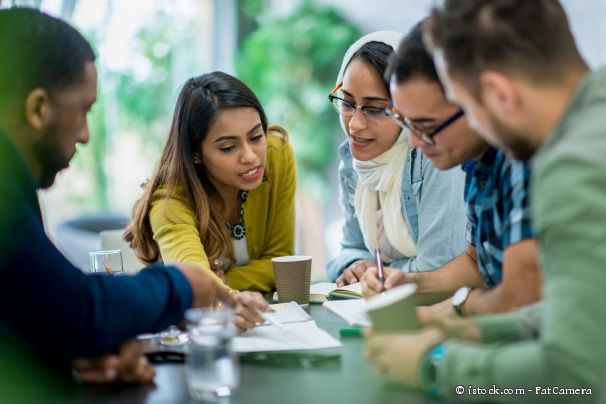 Fünf Personen sitzen an einem Tisch zusammen und sprechen über eine Broschüre, die in der Mitte des Tisches liegt.