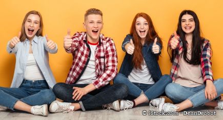 Vier Schüler sitzen nebeneinander im Schneidersitz und zeigen freudig ihre Daumen hoch.