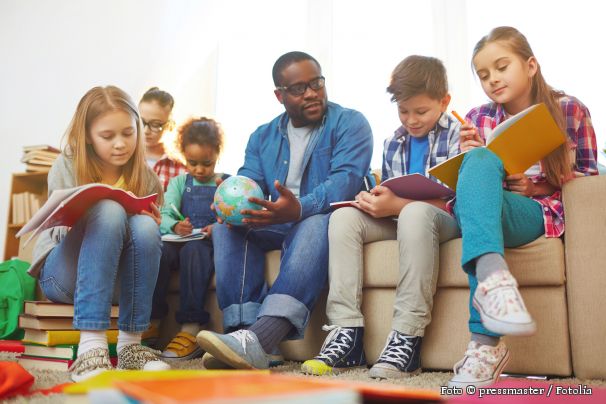 ein Lehrer sitzt gemeinsam mit Schülern auf einem Sofa und unterrichtet.