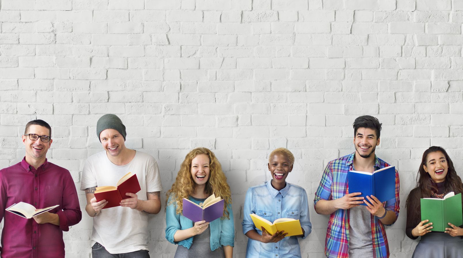 Sechs Personen stehen nebeneinander an einer Wand, lachen und halten ein Buch in der Hand.